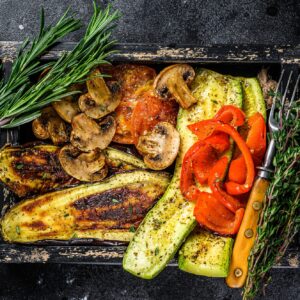 Baked vegetables bell pepper, zucchini, eggplant and tomato in a wooden tray.
